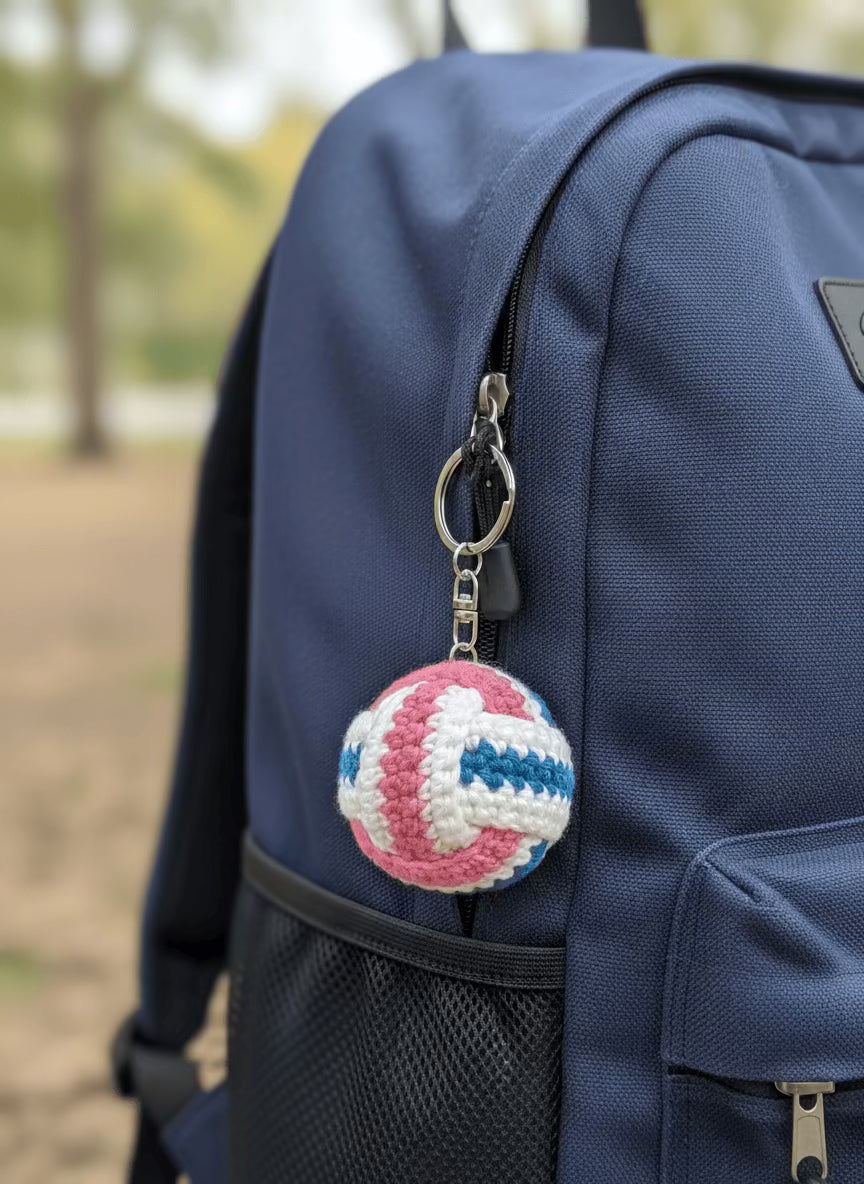 Crocheted volleyball keychain in pink, blue, and white on a plain background